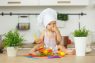 Baby in the cook costume in the white hat with vegetables